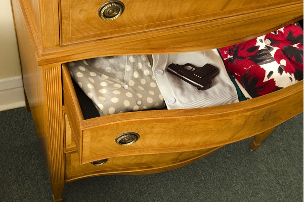open dresser drawer with gun sitting on top of folded clothing