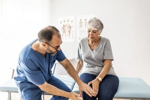 male doctor examining older adult woman's knee to determine cause of pain