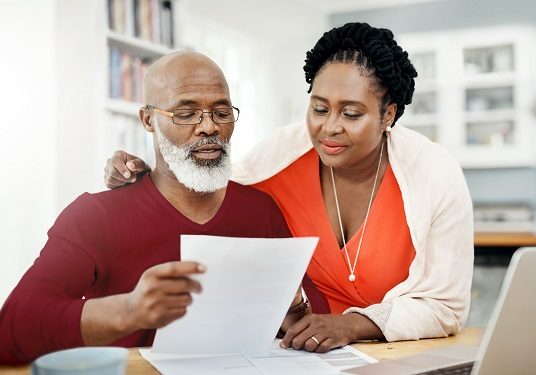 image of mature couple reviewing paperwork together at home on their kitchen table